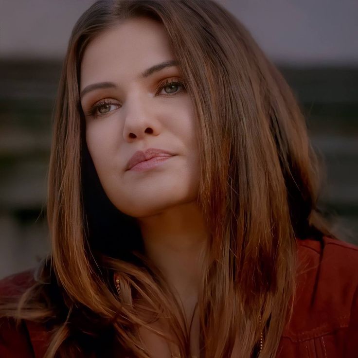 a woman with long brown hair looking off to the side and wearing a red shirt