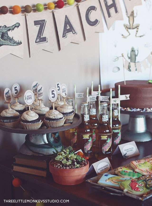 a table topped with cupcakes and cakes covered in frosting next to bottles of beer