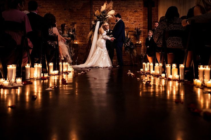 a bride and groom standing at the end of their wedding ceremony with candles in front of them