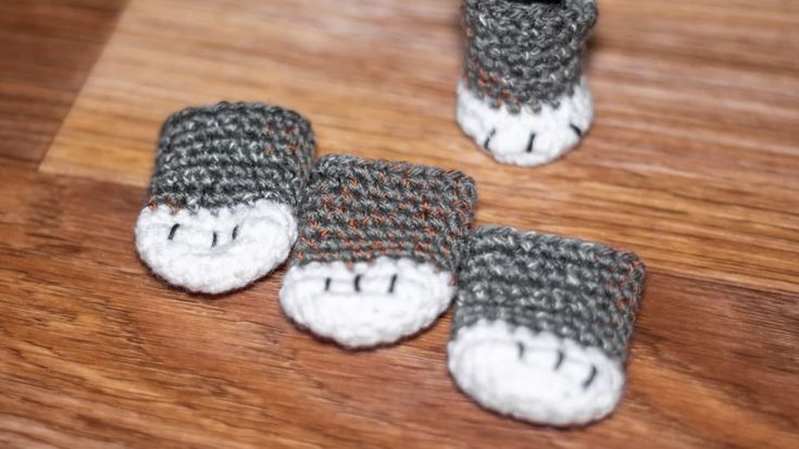 three crocheted slippers are sitting on a wooden surface, one is grey and the other is white