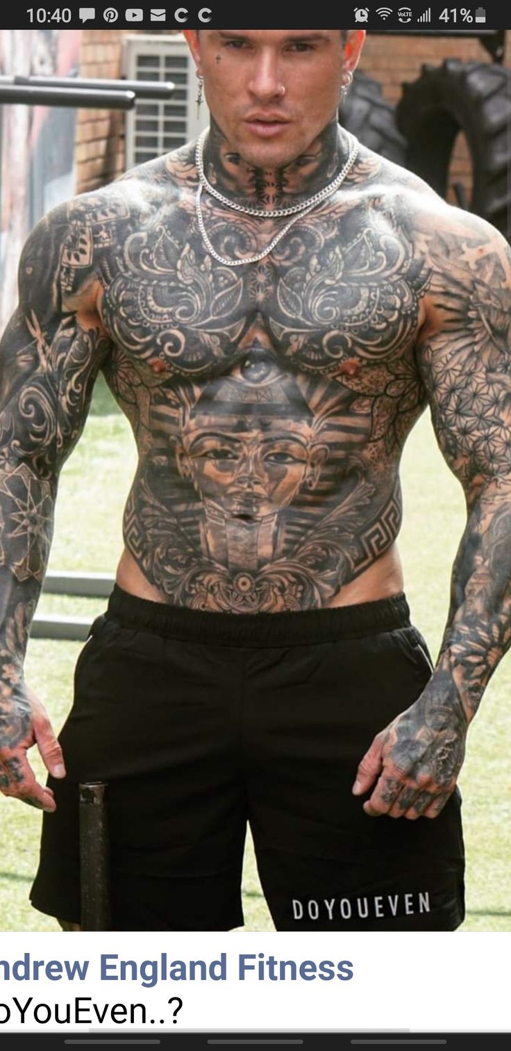 a man with tattoos on his chest standing in front of a fence and looking at the camera