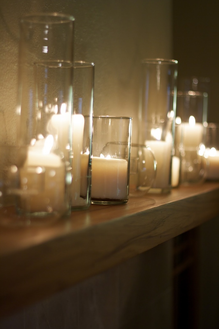 candles are lined up on a mantle with glass vases