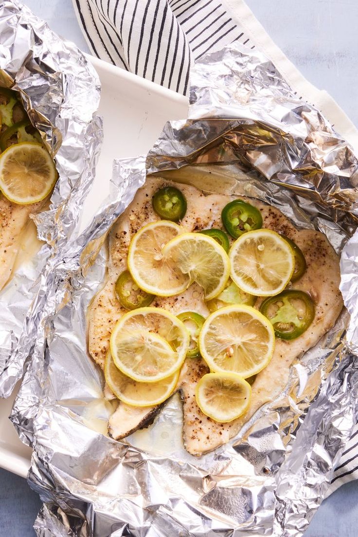 two pieces of fish covered in lemons and jalapenos on tin foil