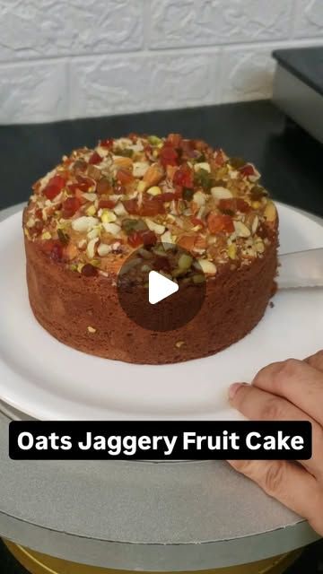 a person cutting into a cake on top of a white plate with the words oats jagery fruit cake