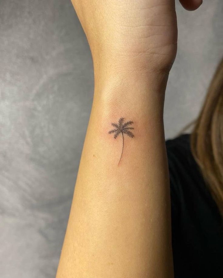 a small palm tree tattoo on the left inner arm and wrist is shown in front of a woman's right hand