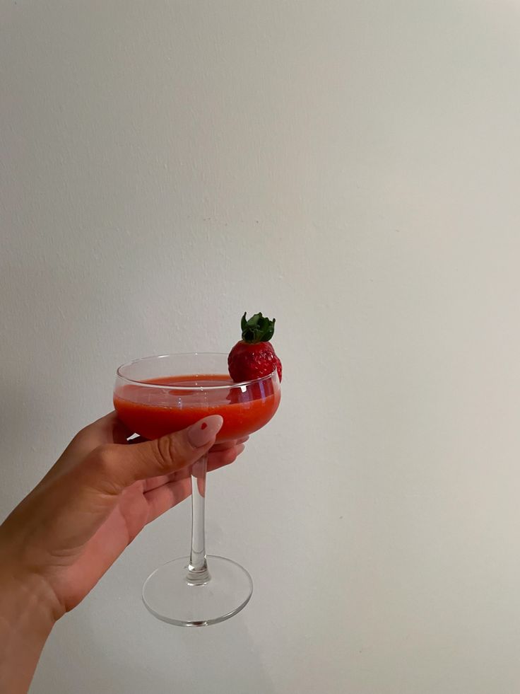 a hand holding a wine glass with a strawberry in it and a red liquid inside