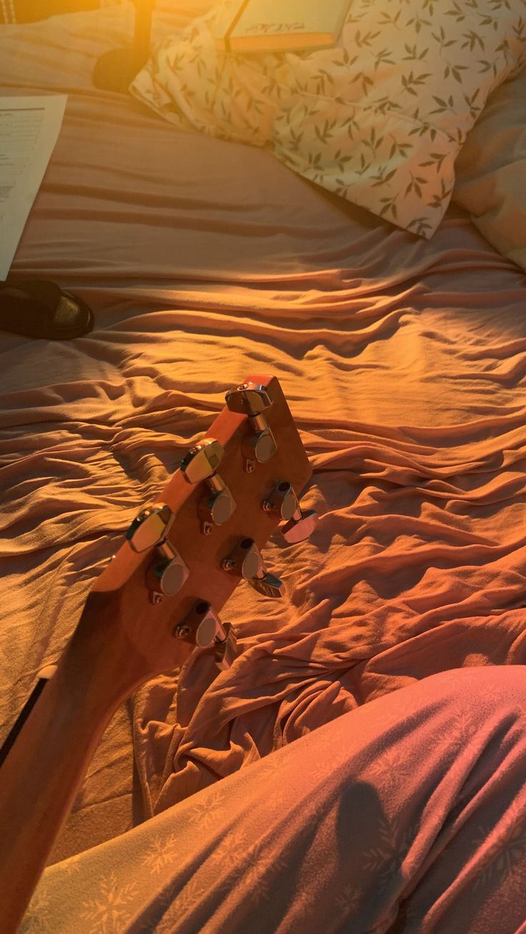 a guitar laying on top of a bed next to pillows