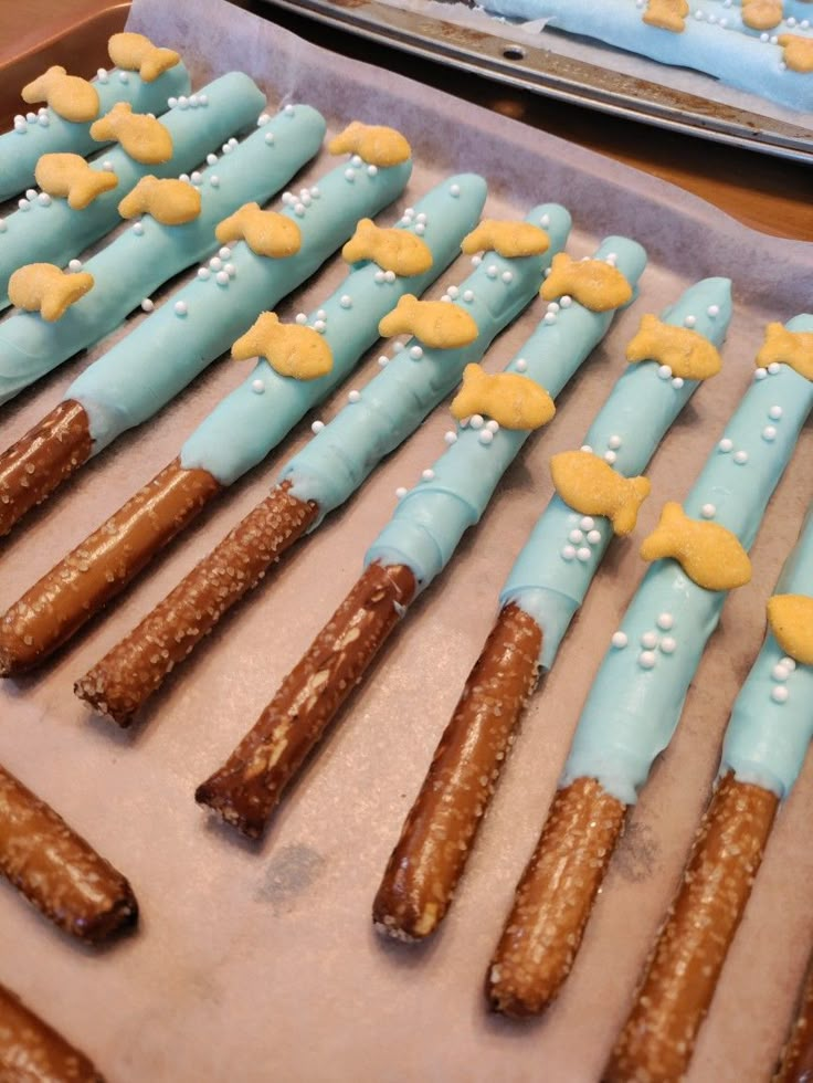 White chocolate dipped pretzel rods with white sprinkles and goldfish crackers on them. The white chocolate is dyed aqua blue. Food Ideas For Fishing Theme Party, The Big One Wave First Birthday Food, The Big One Food Ideas, Ofishally Five Birthday, Ofishally One Birthday Food Ideas, The Big One Surf Birthday Food Ideas, 1st Birthday Boy Fishing Theme, The Big One Party Favors, The Big One Surf Birthday Food