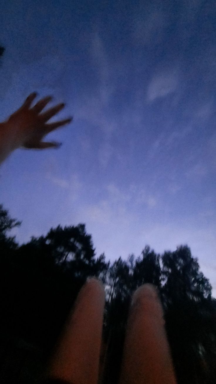 someone is holding their hand out in front of the sky with trees and clouds behind them