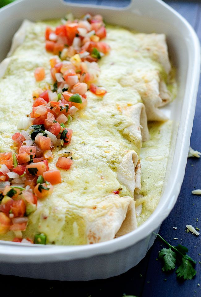 an enchilada in a white casserole dish with tomatoes and cilantro