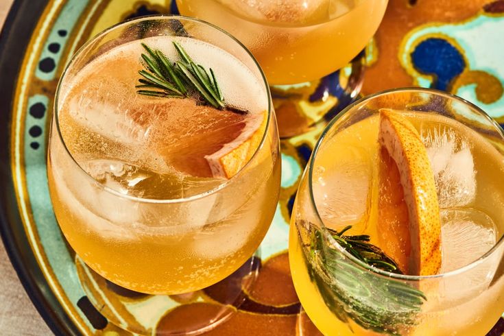 two glasses filled with drinks sitting on top of a blue and yellow plate topped with orange slices