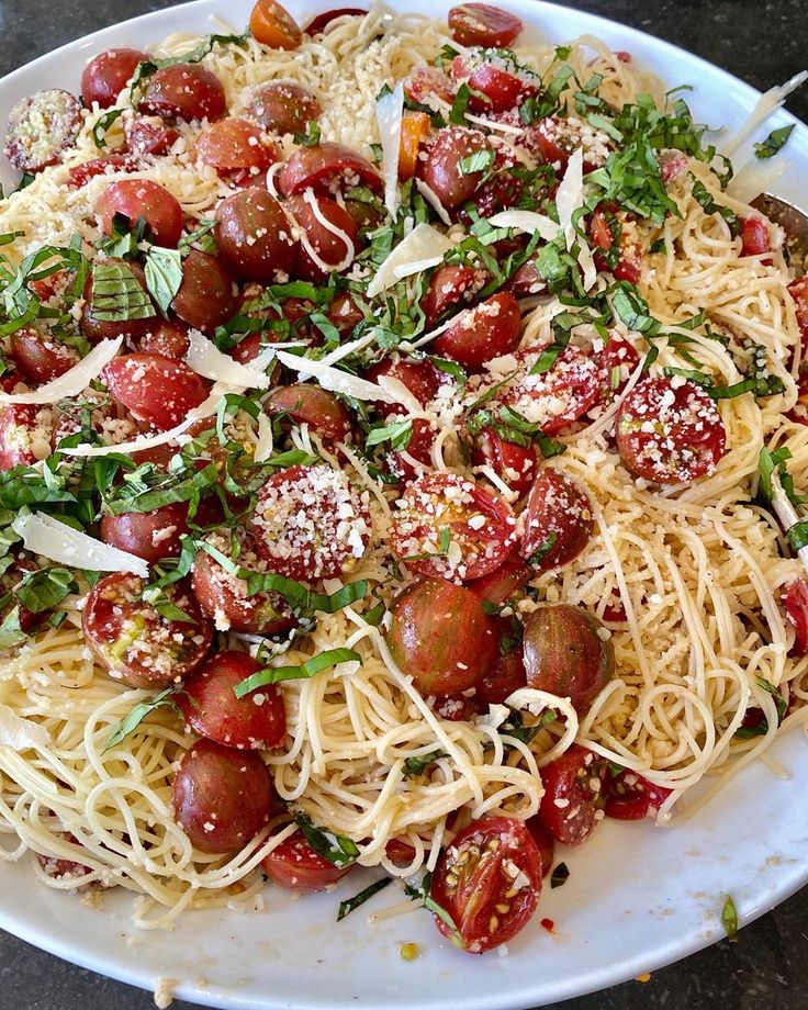 a white plate topped with pasta covered in tomatoes and parmesan sprinkles