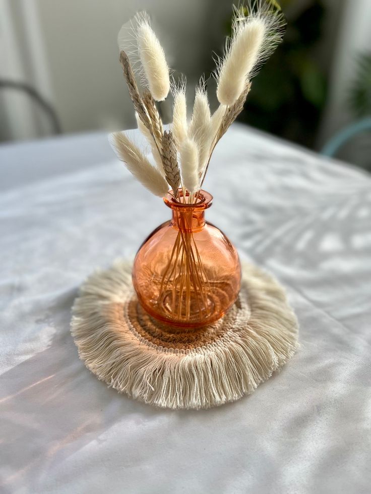 a glass vase with feathers in it sitting on a white table cloth covered tablecloth