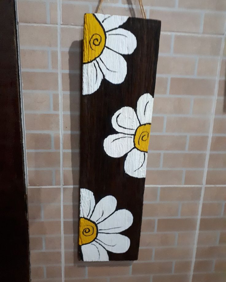 a wooden sign with white and yellow flowers painted on it hanging from a brick wall