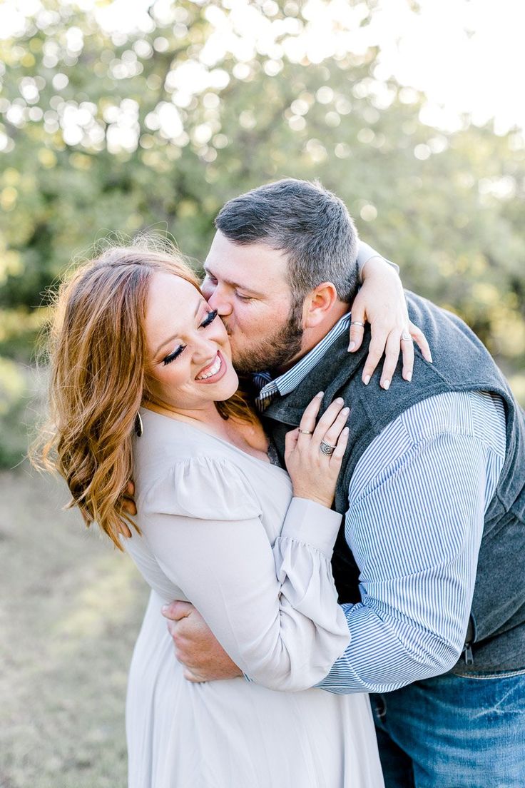 a man and woman embracing each other in front of the camera with trees behind them