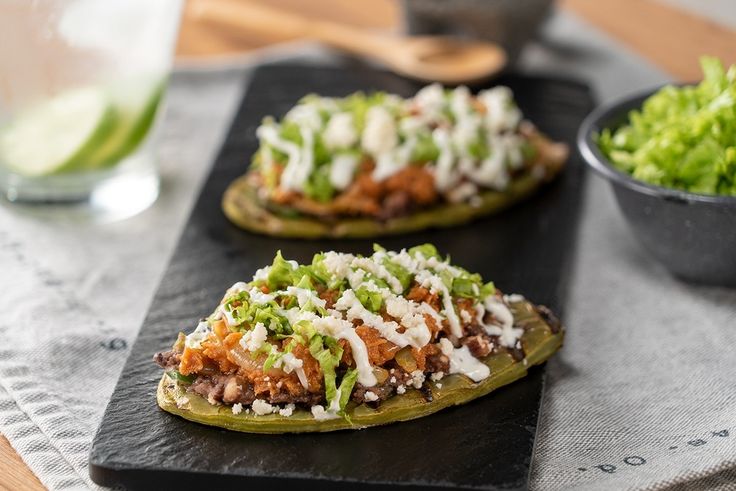 three stuffed peppers with cheese and lettuce on a cutting board next to a glass of water