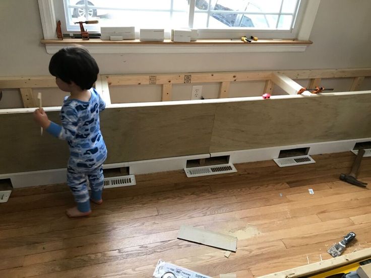 a little boy standing on the floor in front of a window with construction tools around him