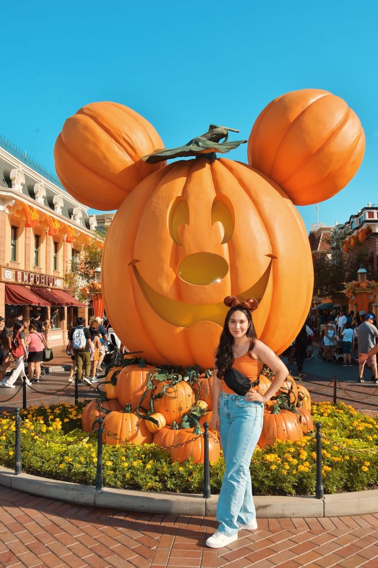 a woman standing in front of a mickey mouse pumpkin