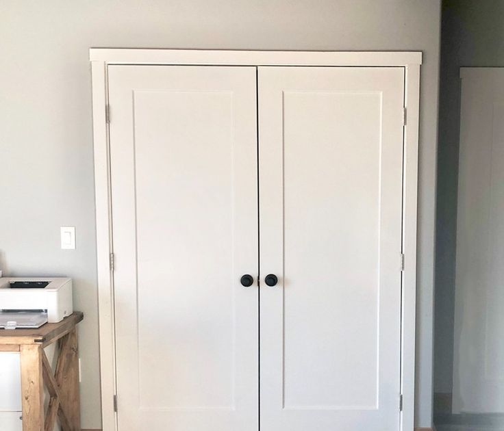 a white closet with two doors and a printer on the floor in front of it