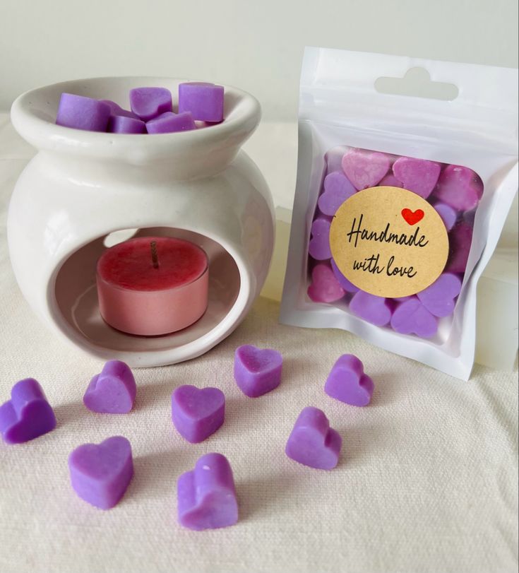 purple hearts are next to a small white vase with a candle in it and a bag of heart shaped candles