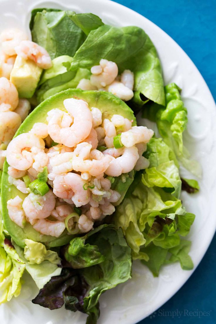 shrimp salad with lettuce and avocado on a white plate against a blue background