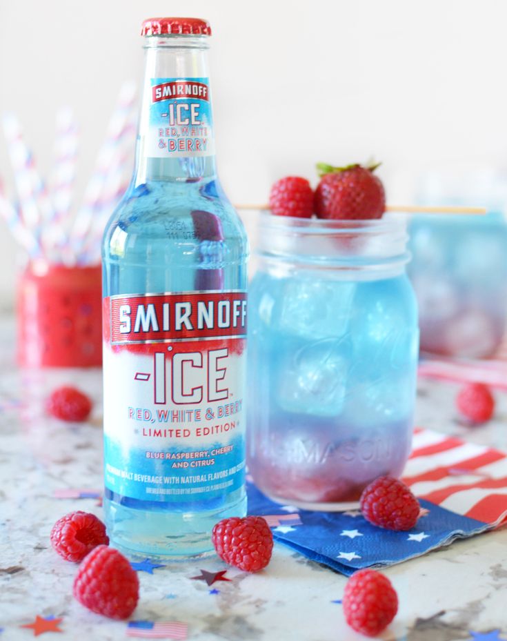 a bottle of ice water with raspberries and strawberries on the table next to it