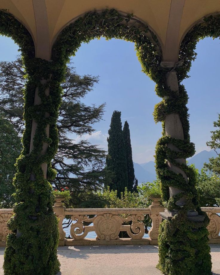 an arch covered in green plants next to trees