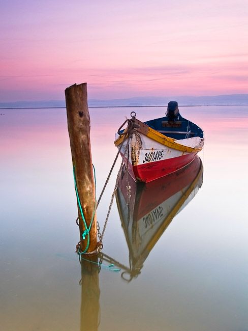 a small boat sitting on top of a body of water next to a wooden pole