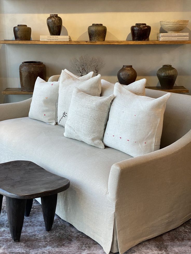 a white couch with pillows on it in front of some vases and other decorative items