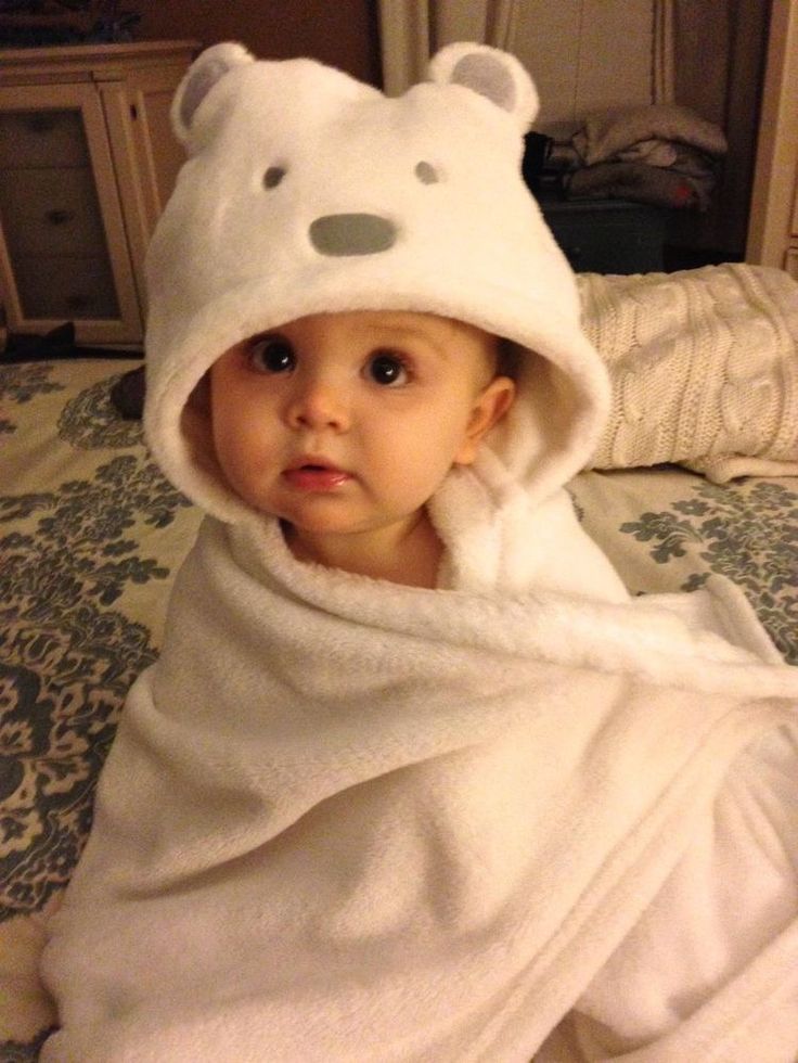 a baby wrapped in a towel on top of a bed with a teddy bear hat