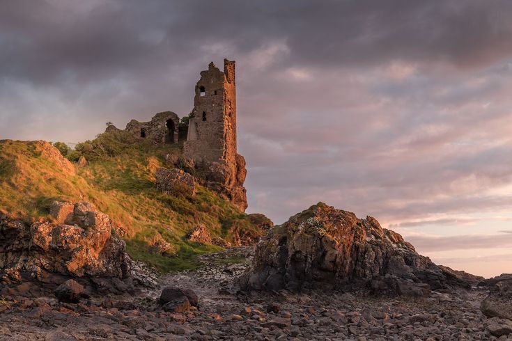 an old castle sits on top of a rocky hill near the ocean at sunset or dawn