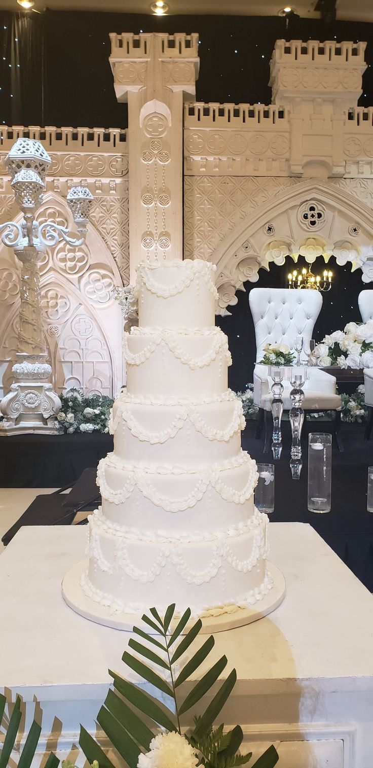 a large white wedding cake sitting on top of a table next to chairs and tables