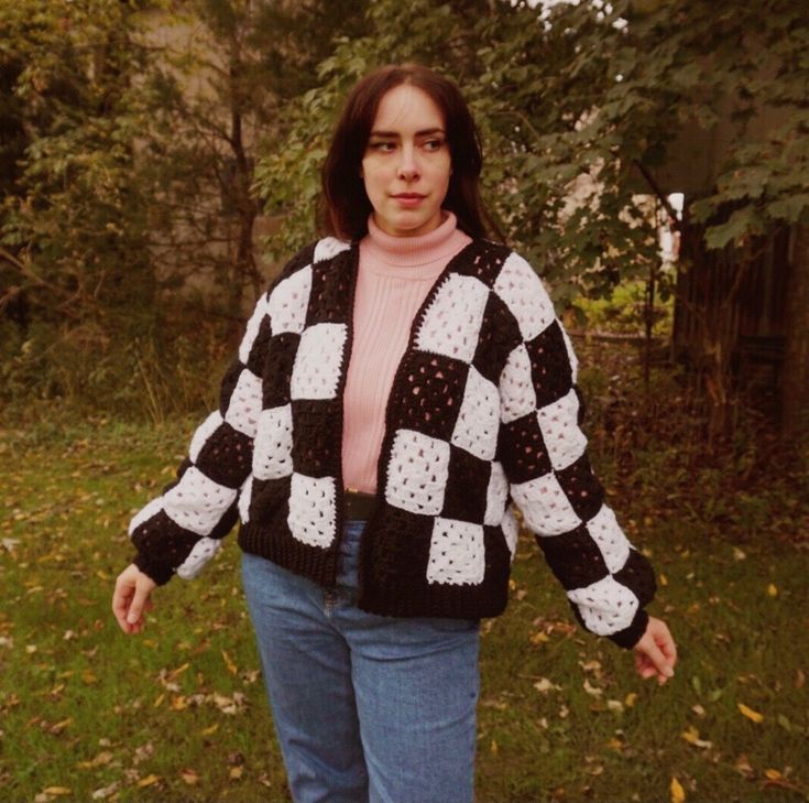 a woman is standing in the grass wearing a black and white checkered cardigan