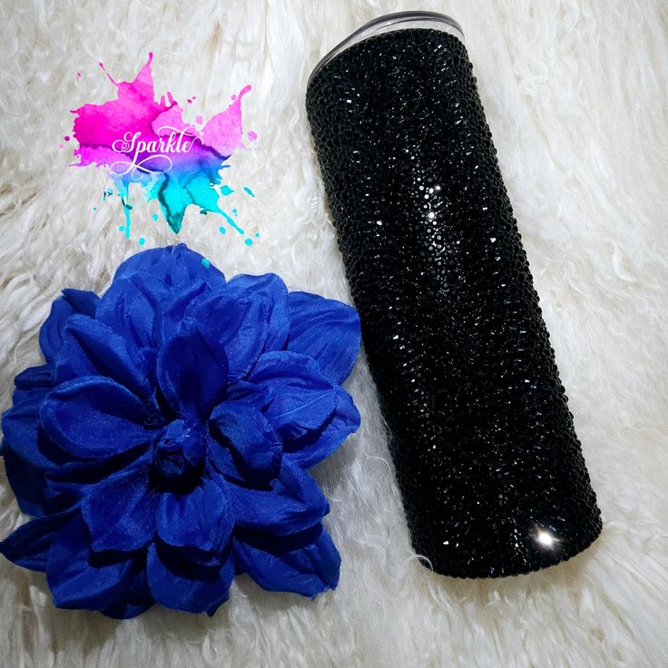 a blue flower next to a black glittered canister on a white fur rug