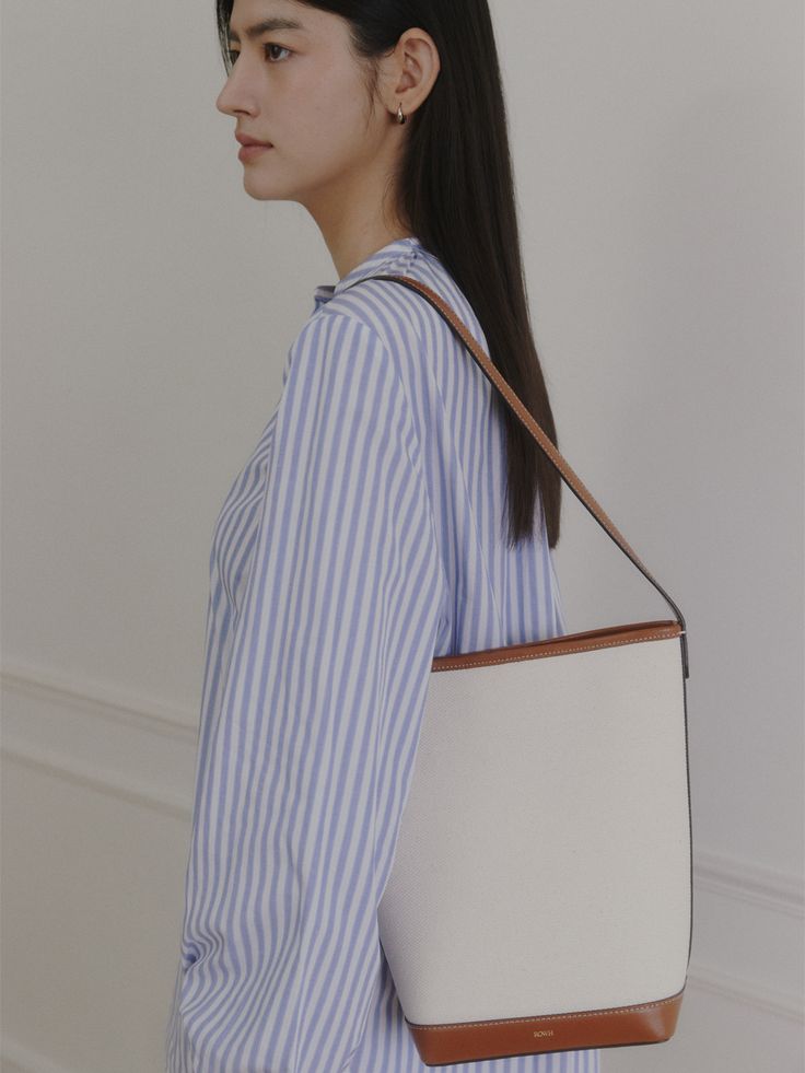 Editor's NoteROWH presents a timeless design that complements a variety of outfits.- Minimal bucket type bag- One handle, medium-sized shopper bag- Classic and spacious design- Inner open pocket detailMeasurements(in.)- Size: 10.24 in. * 10.83 in. * 4.72 in.- Strap: 10.24 in. Composition & Care- Upper: 100% Cotton, 100% Cow Leather / Lining: 65% Polyester, 35% Cotton / Strap: Cow Leather- Natural leather may have fine scratches and wrinkles- Bright leather can get stained by denim or da Classic Office Tote Bucket Bag, Rectangular Beige Bucket Bag For Work, Rectangular Beige Hobo Bag For Work, Versatile Leather Handles Bucket Bag For Office, Versatile Style Bucket Bag With Leather Handles, Beige Bucket Bag With Leather Handles For Work, Leather Handle Bucket Box Bag For Shopping, Beige Hobo Bag For Work, Versatile Office Bucket Bag With Leather Handles