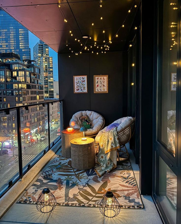 a balcony with two wicker chairs and a table on it in front of the city lights