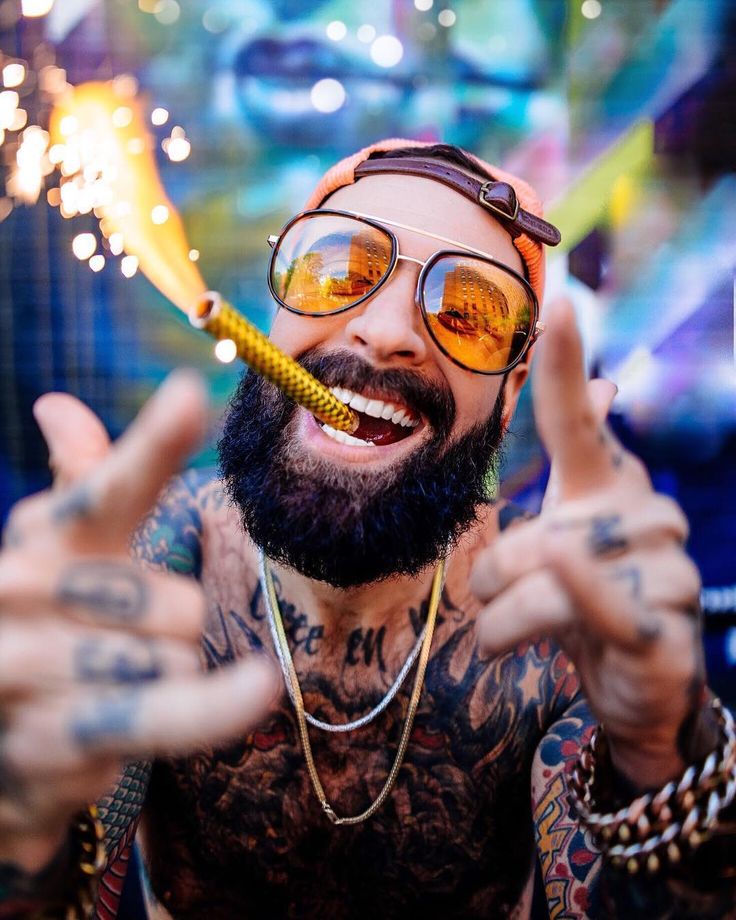 a man with tattoos and glasses holding a sparkler in front of his face while making the peace sign