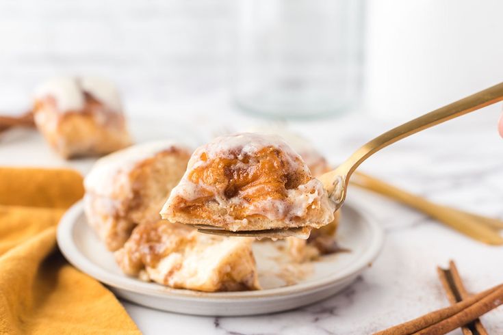 a person holding a spoon with cinnamon rolls on it