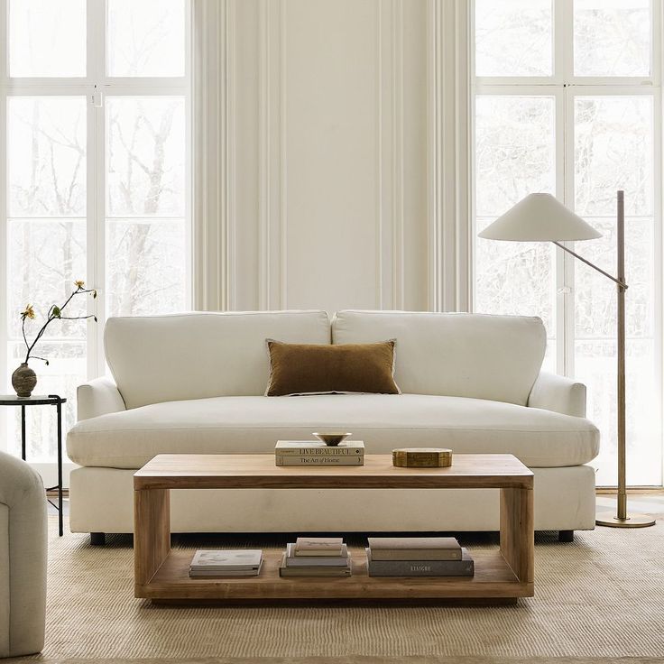 a living room with white couches and tables in front of two large windowed windows