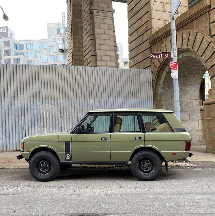 an old green car is parked in front of a wall and street sign that reads pearl st