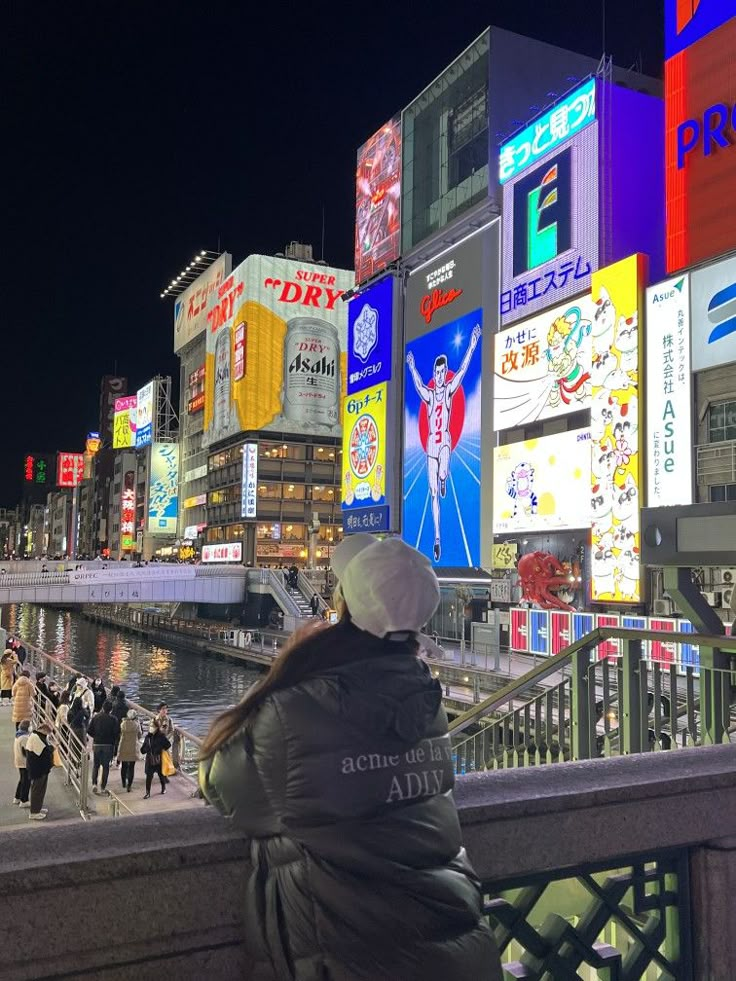 a woman is sitting on a bench looking at the street lights in tokyo, japan