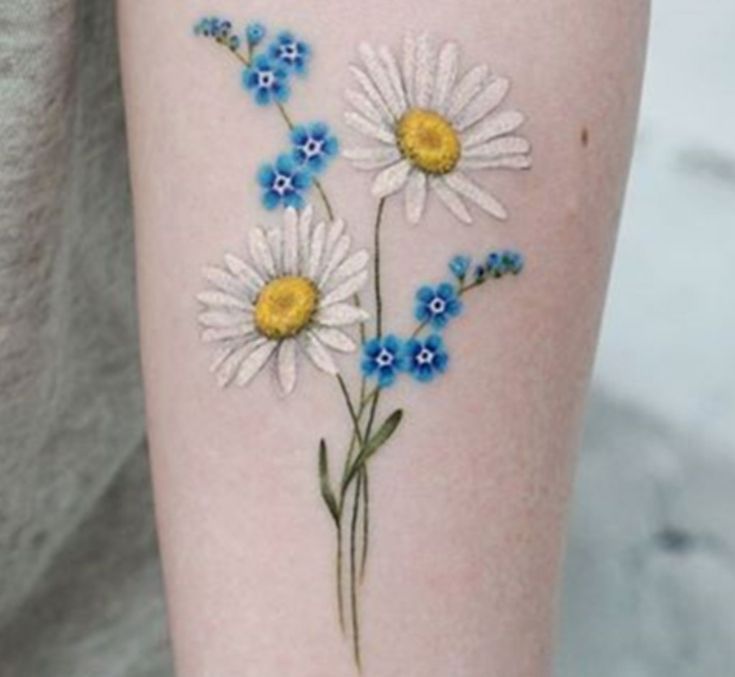 a woman's arm with daisies and blue flowers on it