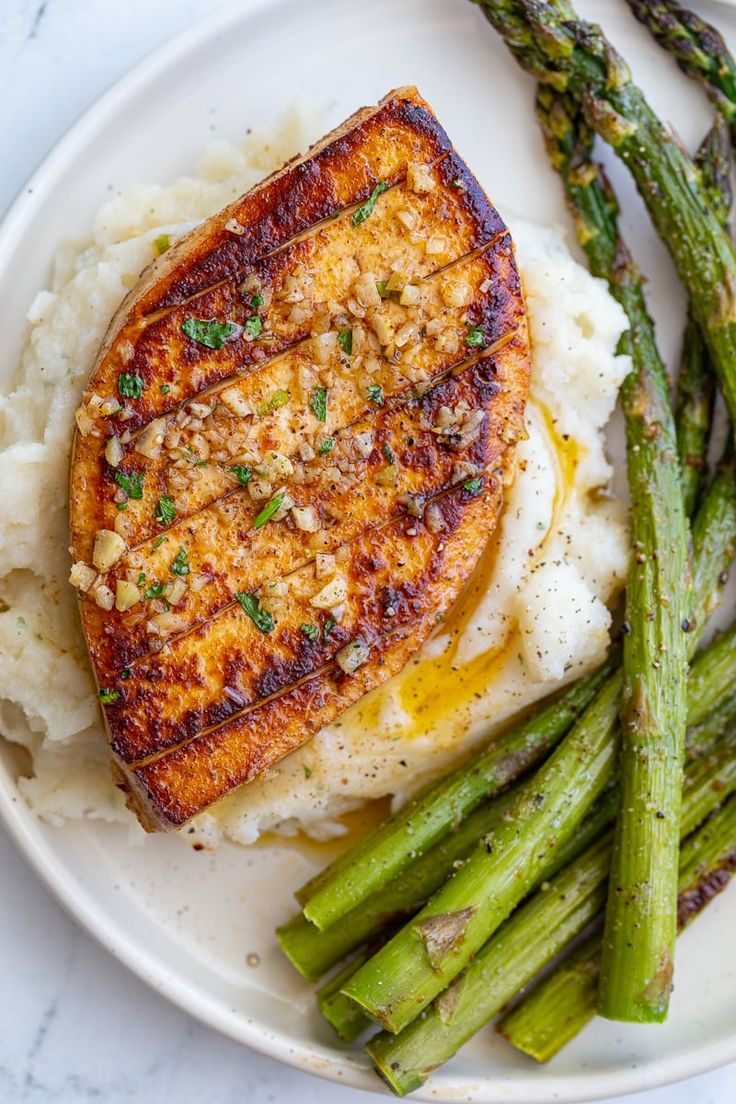 a white plate topped with fish and mashed potatoes next to asparagus spears