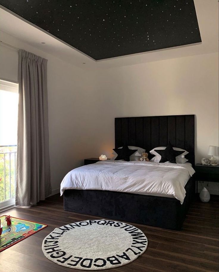 a bedroom with a large bed and stars on the ceiling, next to a window