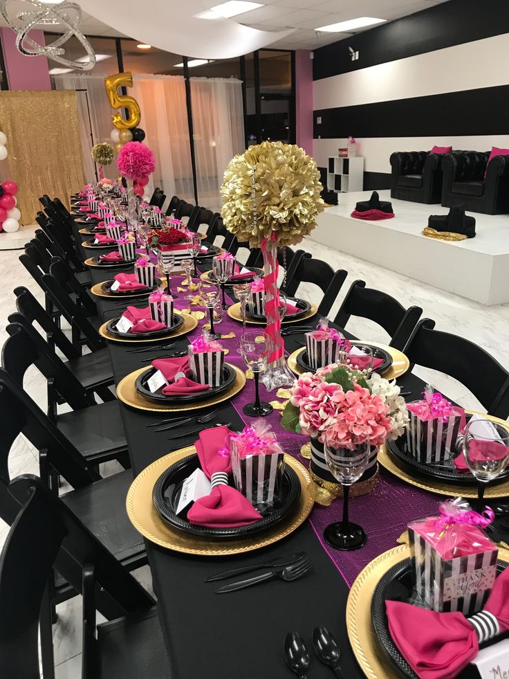 a long table set with black and gold plates, pink napkins, and centerpieces