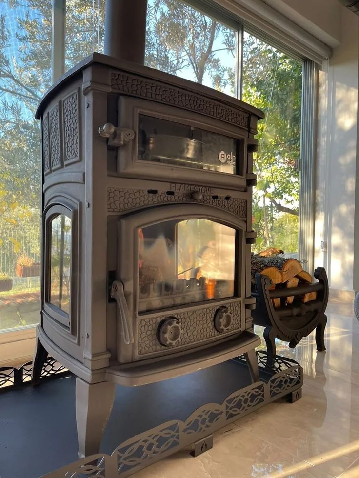 a stove sitting inside of a living room next to a large window on top of a hard wood floor