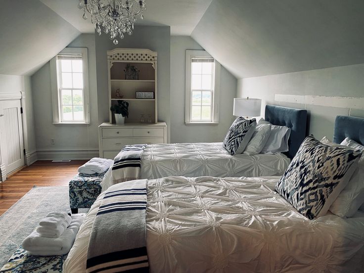 three beds in a room with white walls and wooden floors, one has a chandelier hanging from the ceiling