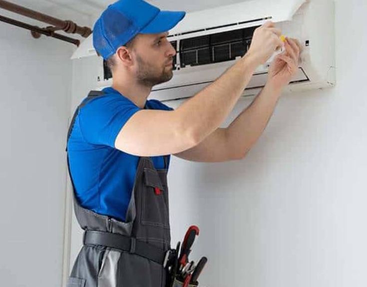 a man working on an air conditioner in a room with tools hanging from the wall