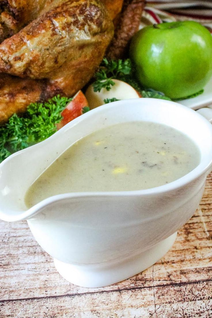 a white gravy bowl filled with soup next to an apple and chicken wings