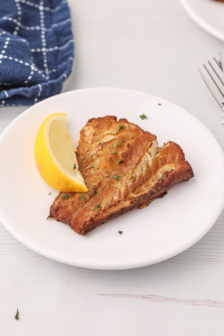 a piece of fish on a white plate with lemon wedges